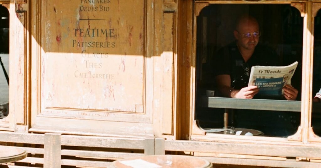 Sunlit outdoor Parisian cafe with a man enjoying a newspaper.