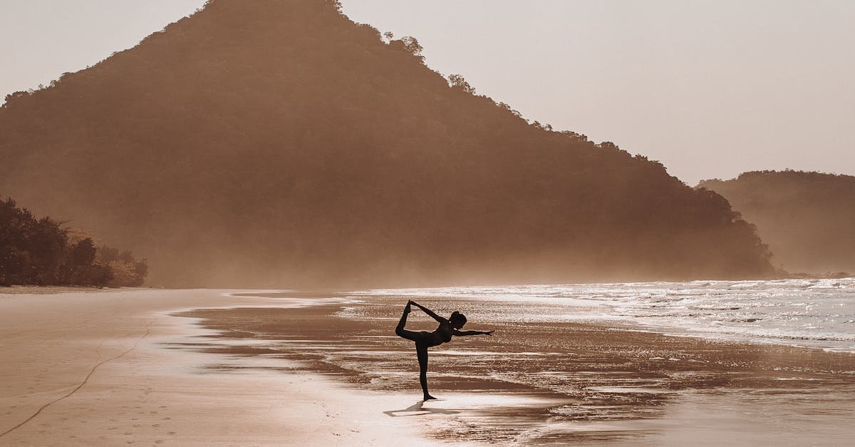 Silhouette of a woman practicing yoga on a tranquil beach during sunrise.