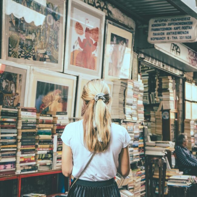 A woman explores a bookshop in an outdoor city market surrounded by books and framed art.