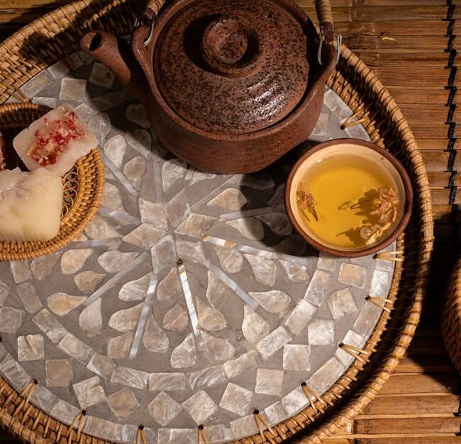 Rustic tea set with herbal tea and traditional Asian snacks arranged on a wooden mat.